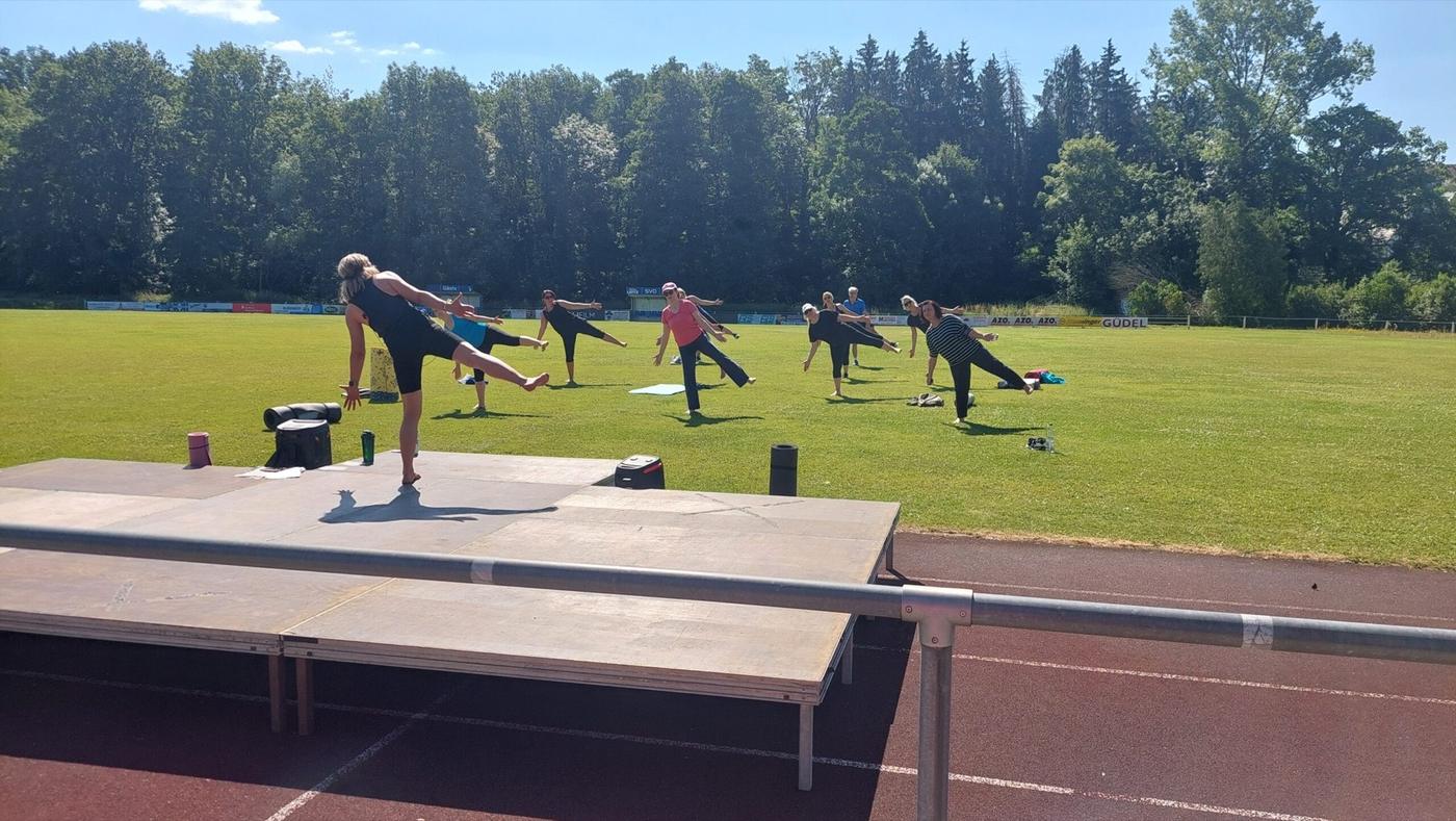 Kursgruppe beim Fitnesstraining auf dem Rasen des Sportplatzes