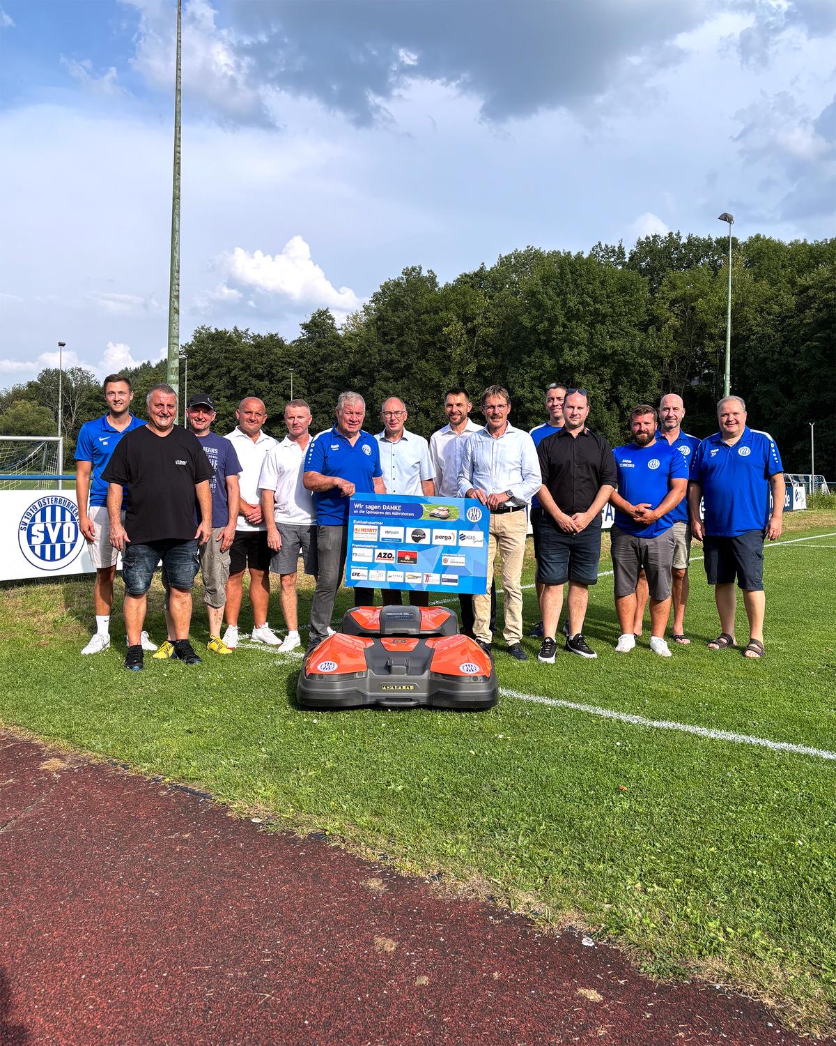 Vereinsvertreter und Sponsoren mit dem neuen Mähroboter auf dem Sportplatz
