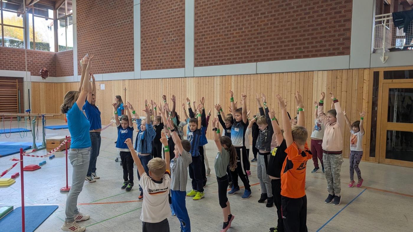 Kinder strecken beim Aufwärmen in der Sporthalle die Arme nach oben